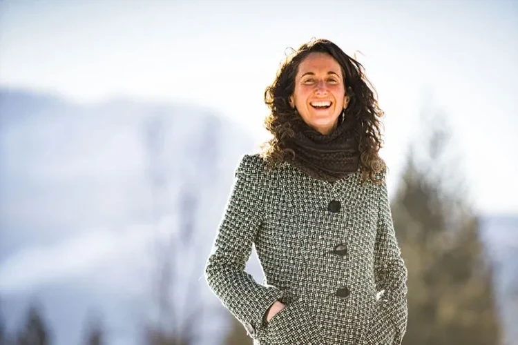 A woman, massage therapist Kim Hayes, standing outside against a backdrop of mountains and trees.